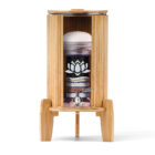 Ein Glas-Wasserfilter mit mehrstufiger Filterkartusche und Edelsteinen, eingefasst in einen Ständer mit Lichtschutz und Deckel aus hellem Bambus.